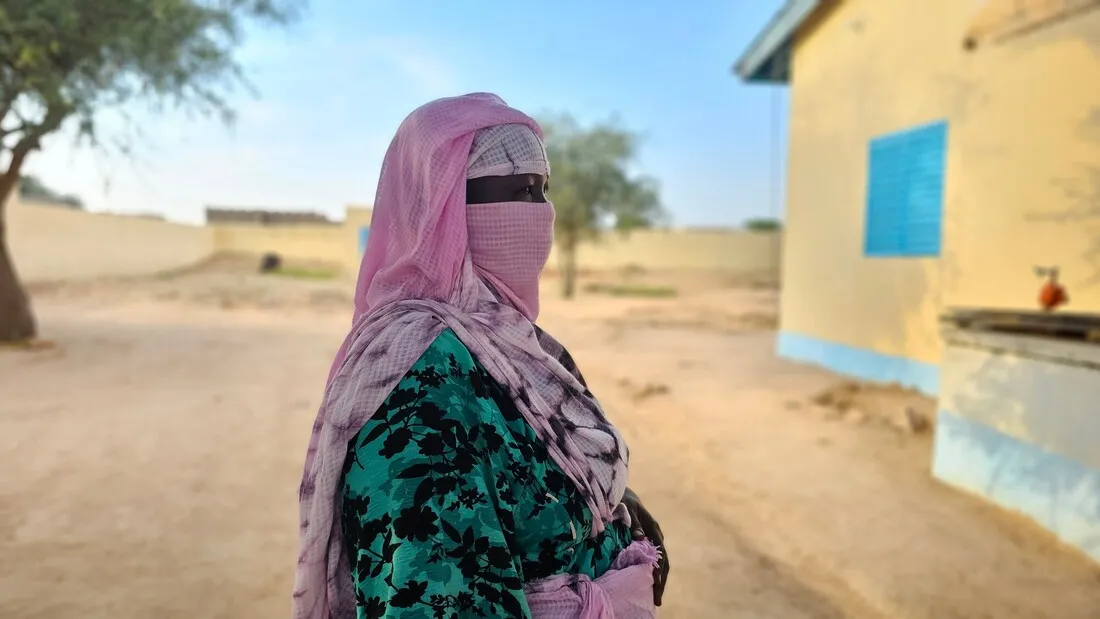 A sideview of a woman from Chad, standing outdoors with a house in the background.