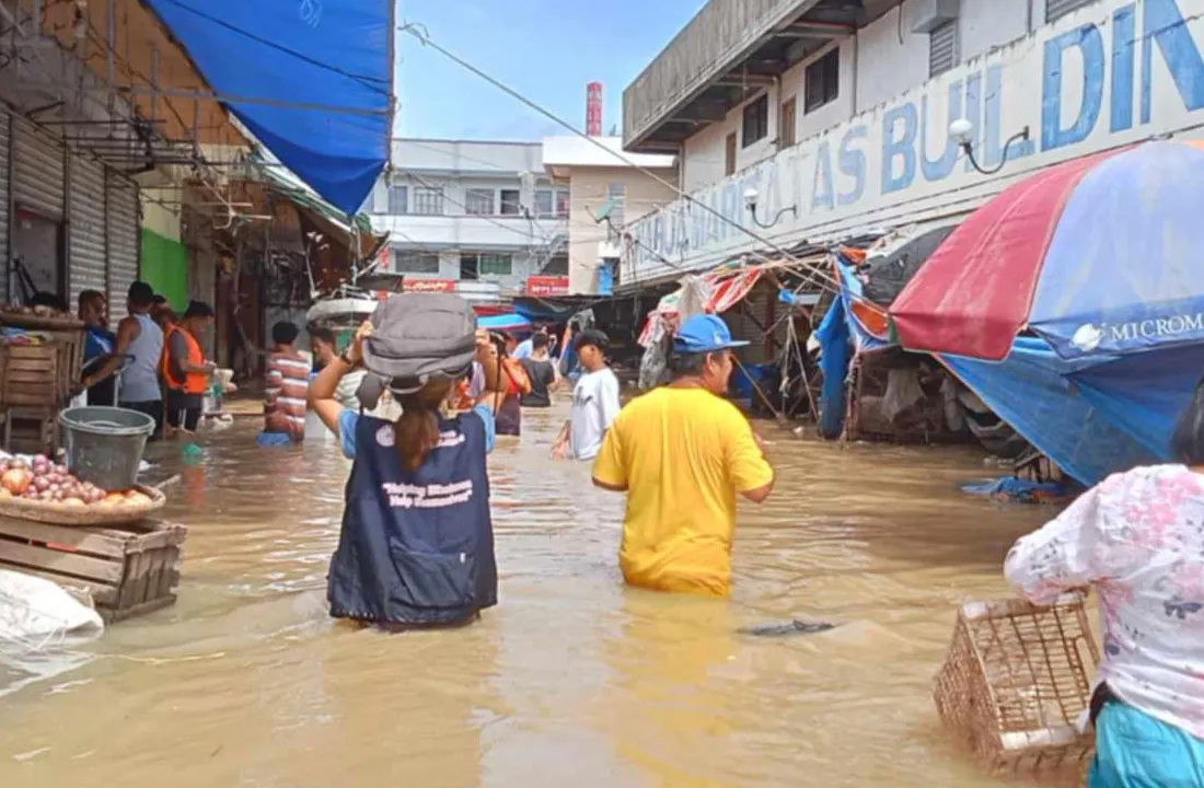 A group of people wade through hip-deep water carrying supplies.